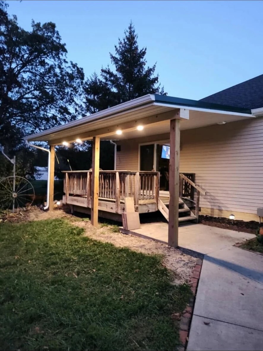 Covered back porch addition with recessed lighting and wood railing